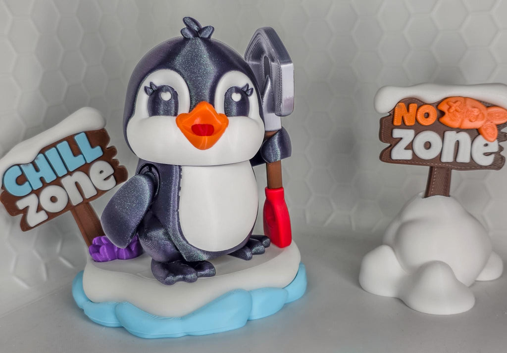 May include: A penguin figurine with a shovel, standing on a snow-covered base. The penguin has a white belly, orange beak, and is flanked by signs that read "Chill Zone" and "No Zone".